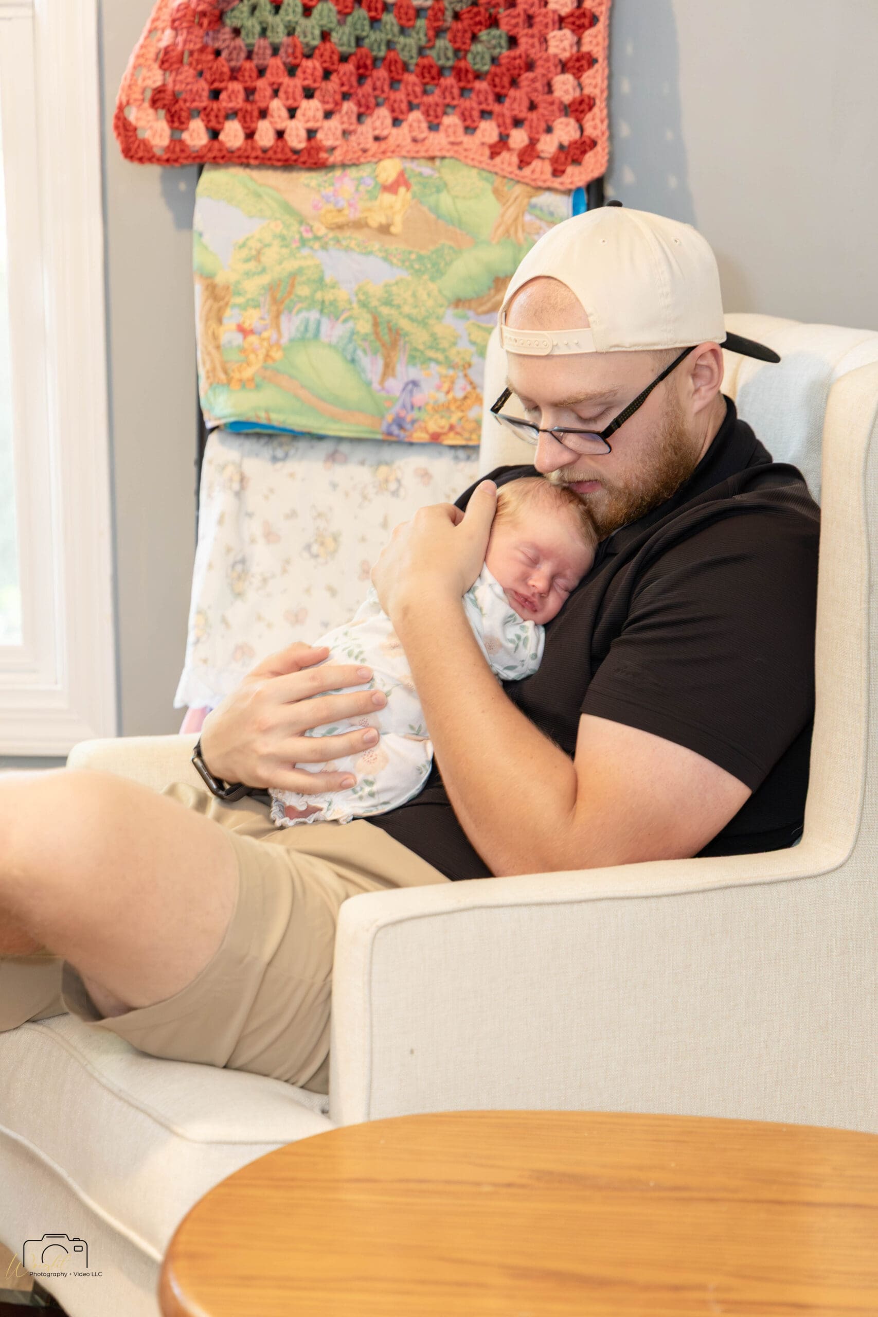 Gage reclined in the rocking chair holding Amelia, wearing his Girl Dad hat