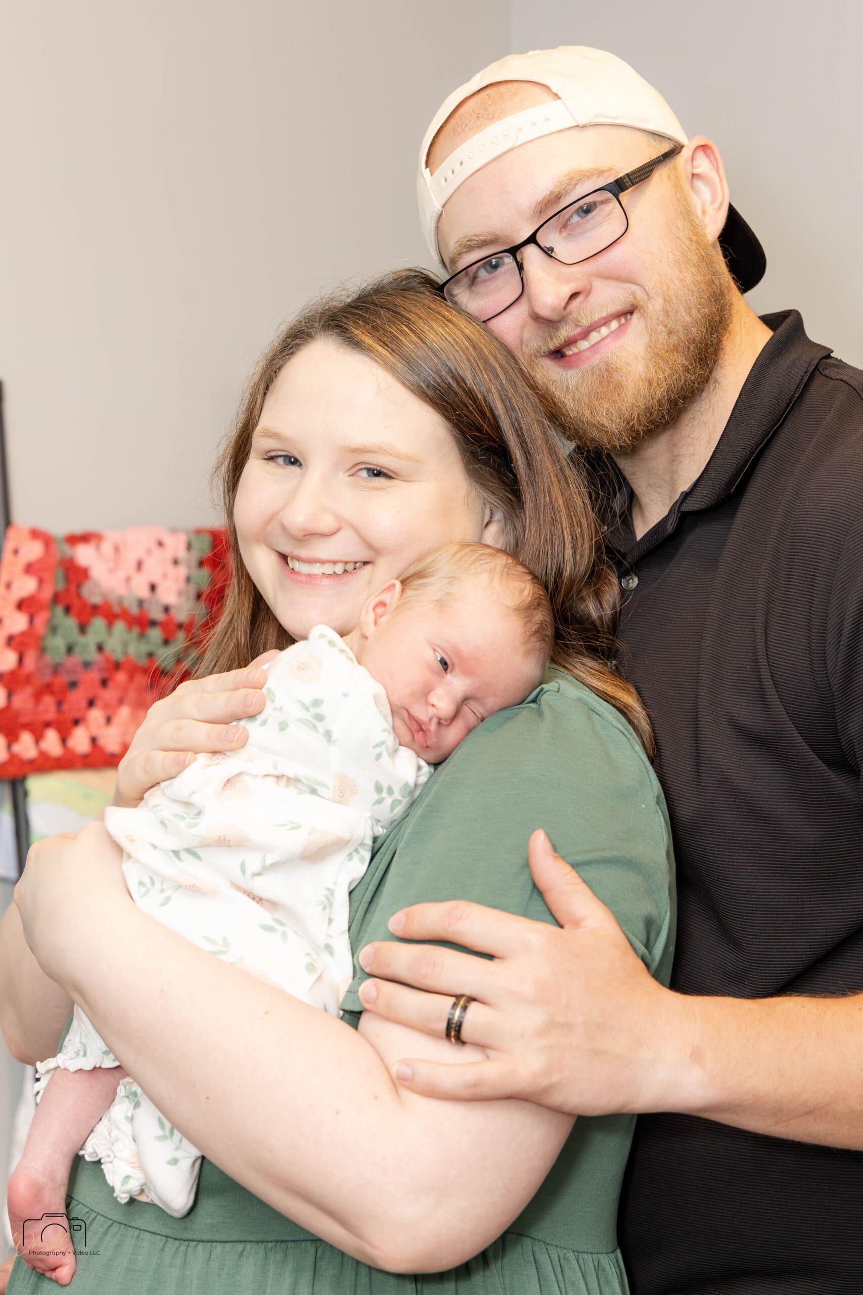 Gage and Emily smiling at the camera while holding baby Amelia