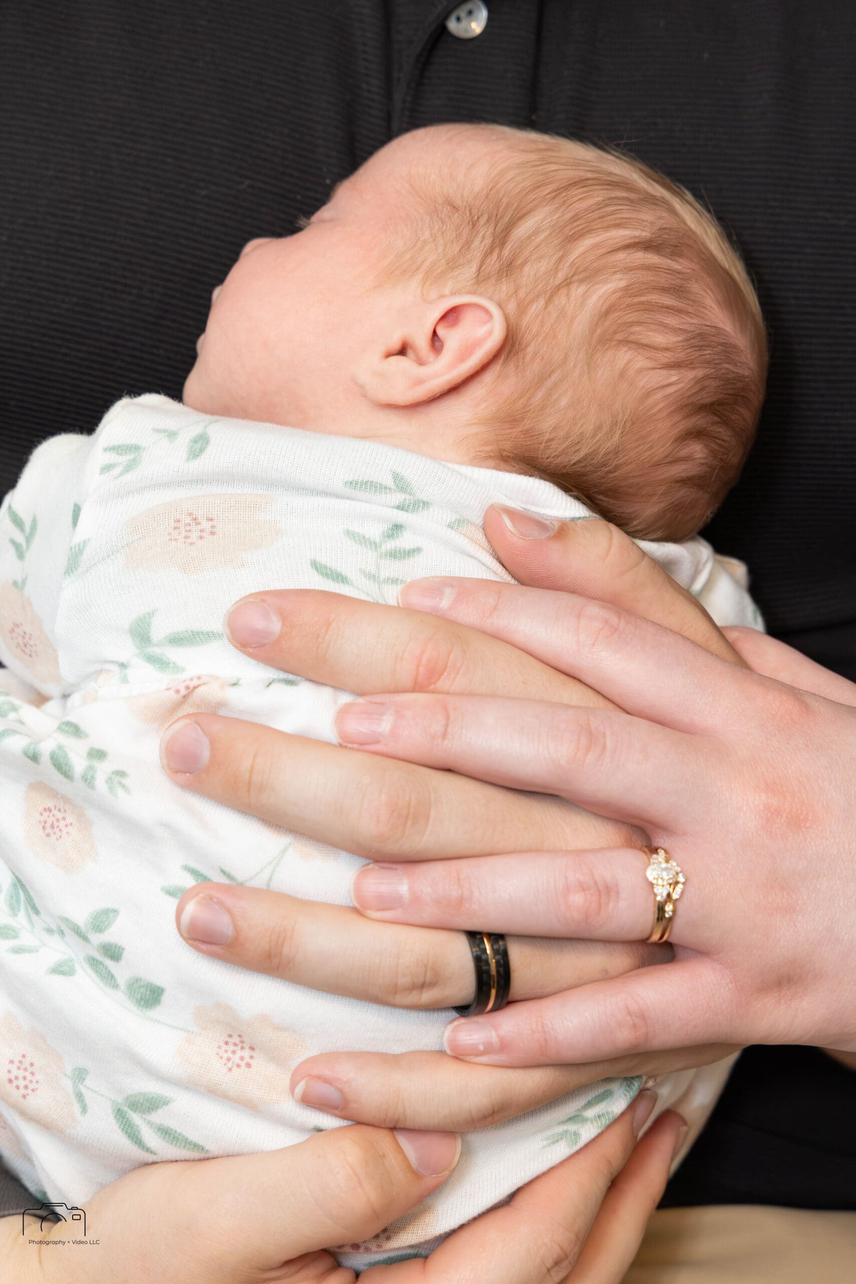 Gage and Emily’s hands resting on baby Amelia, wearing their wedding bands