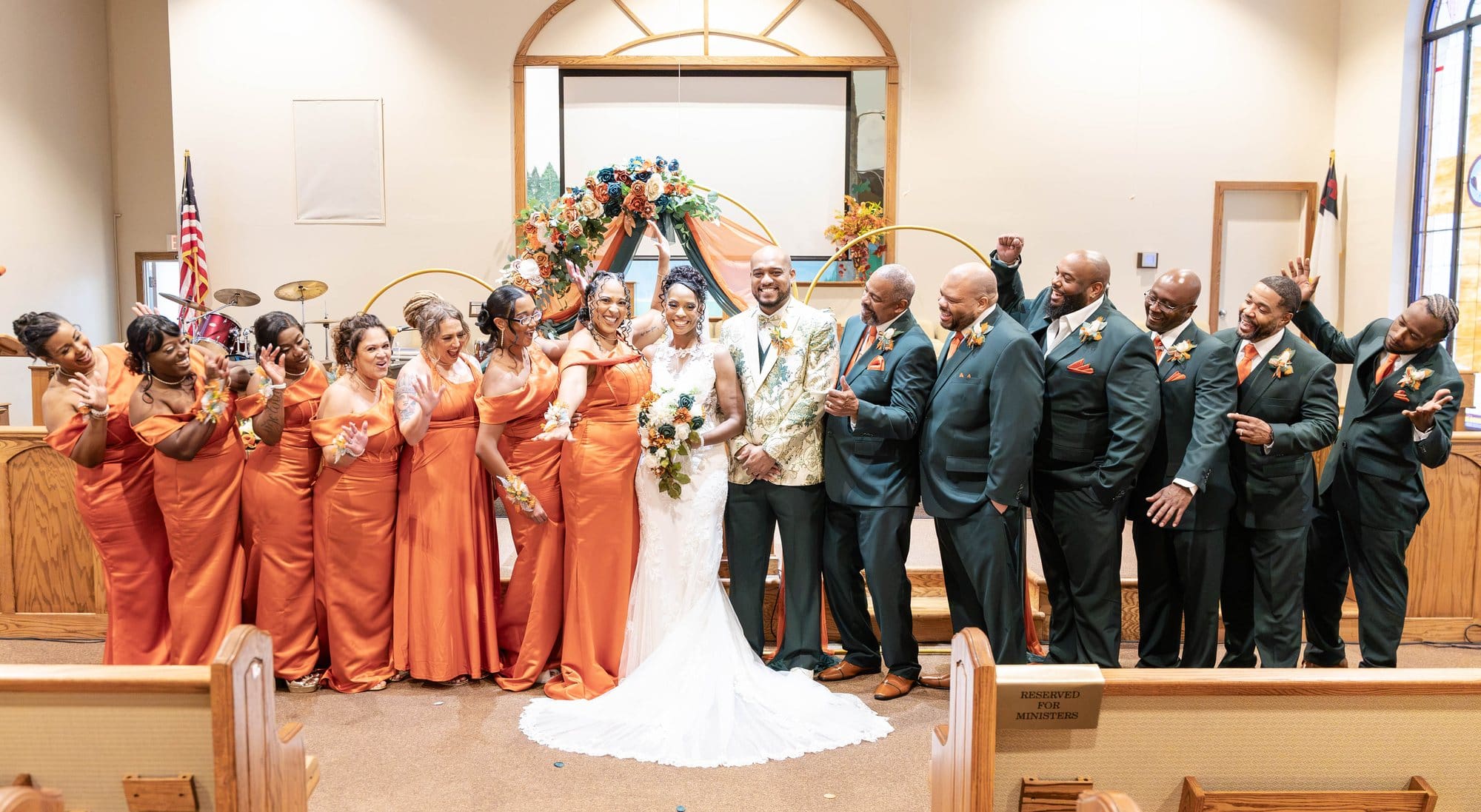 Bridal party in copper satin gowns and emerald suits cheering with the bride and groom at the altar