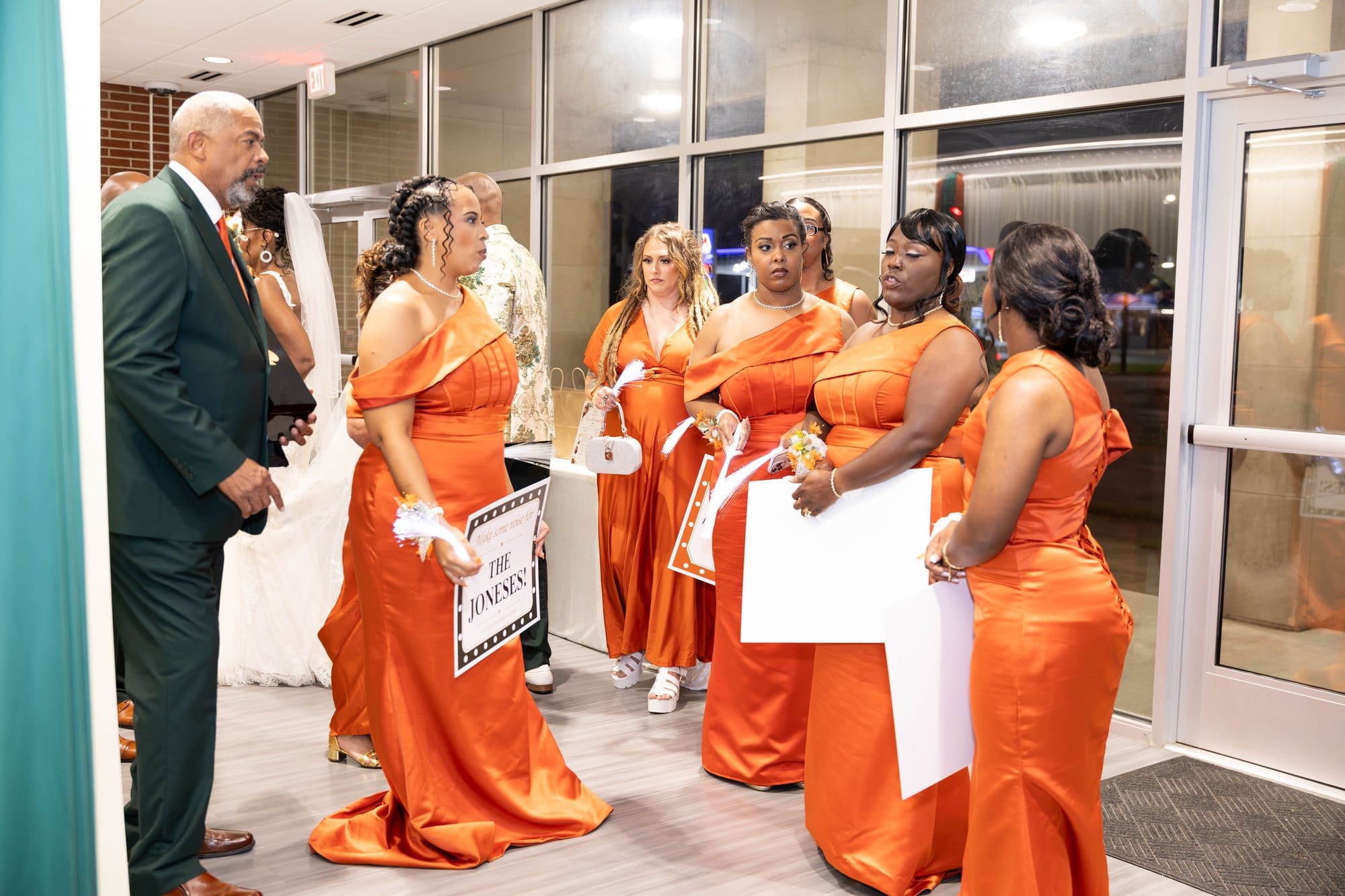 Bridesmaids in copper satin gowns holding marquee signs while they wait at the reception entrance