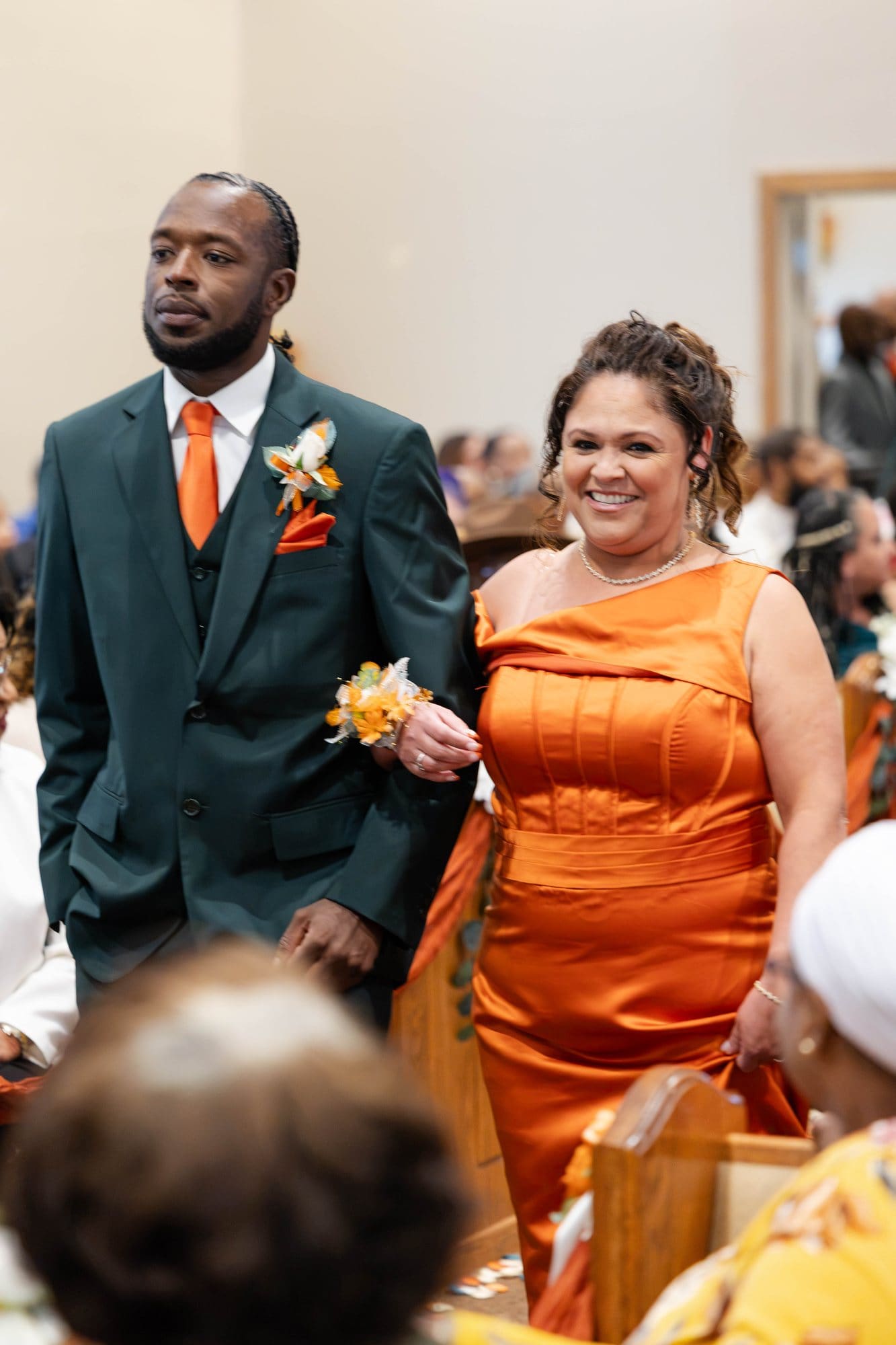 Groomsman and bridesmaid in a copper satin gown walking arm in arm down the church aisle