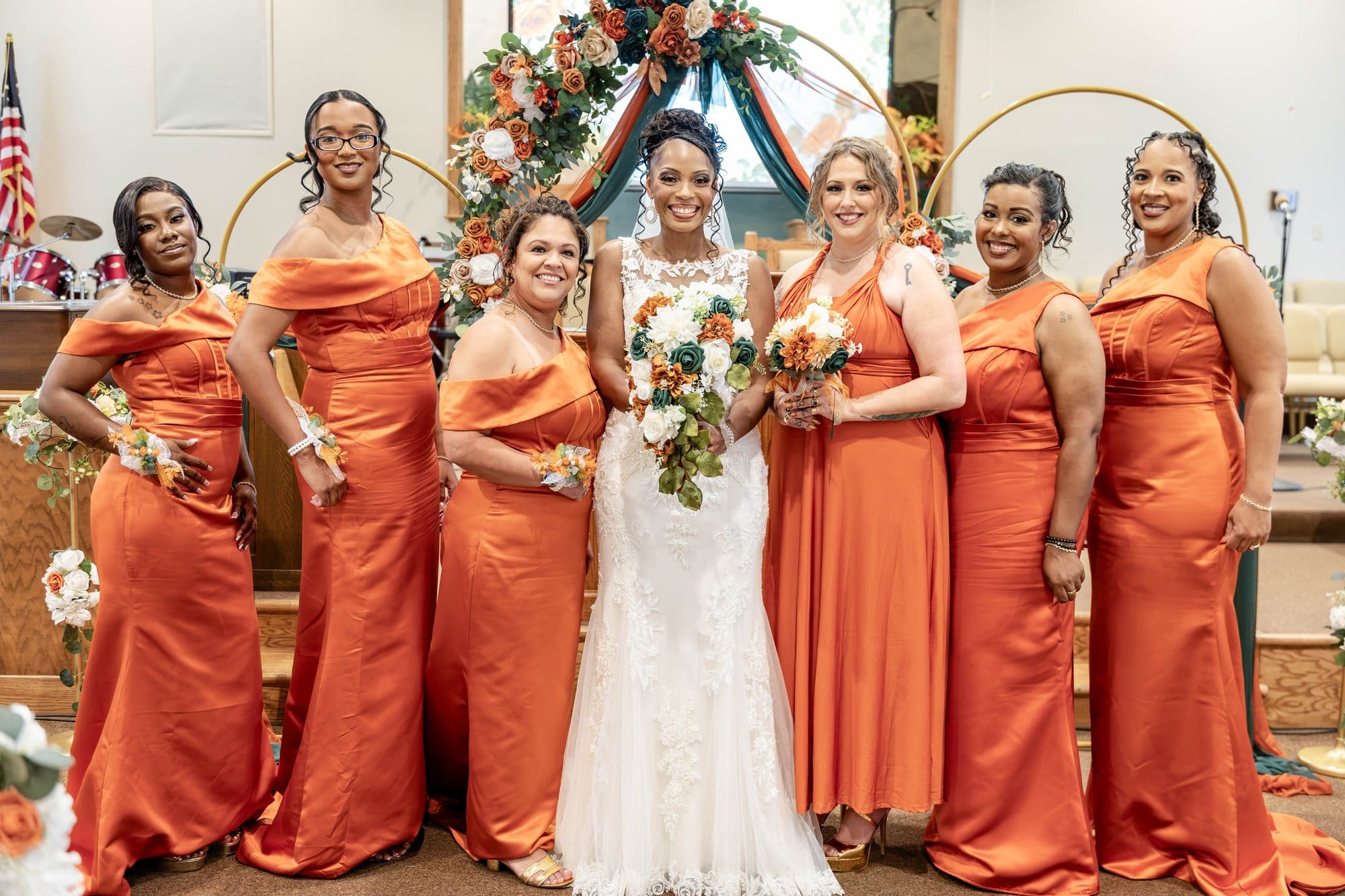 Nikeesha with her bridesmaids in spiced copper satin gowns in front of the gold hoop arch
