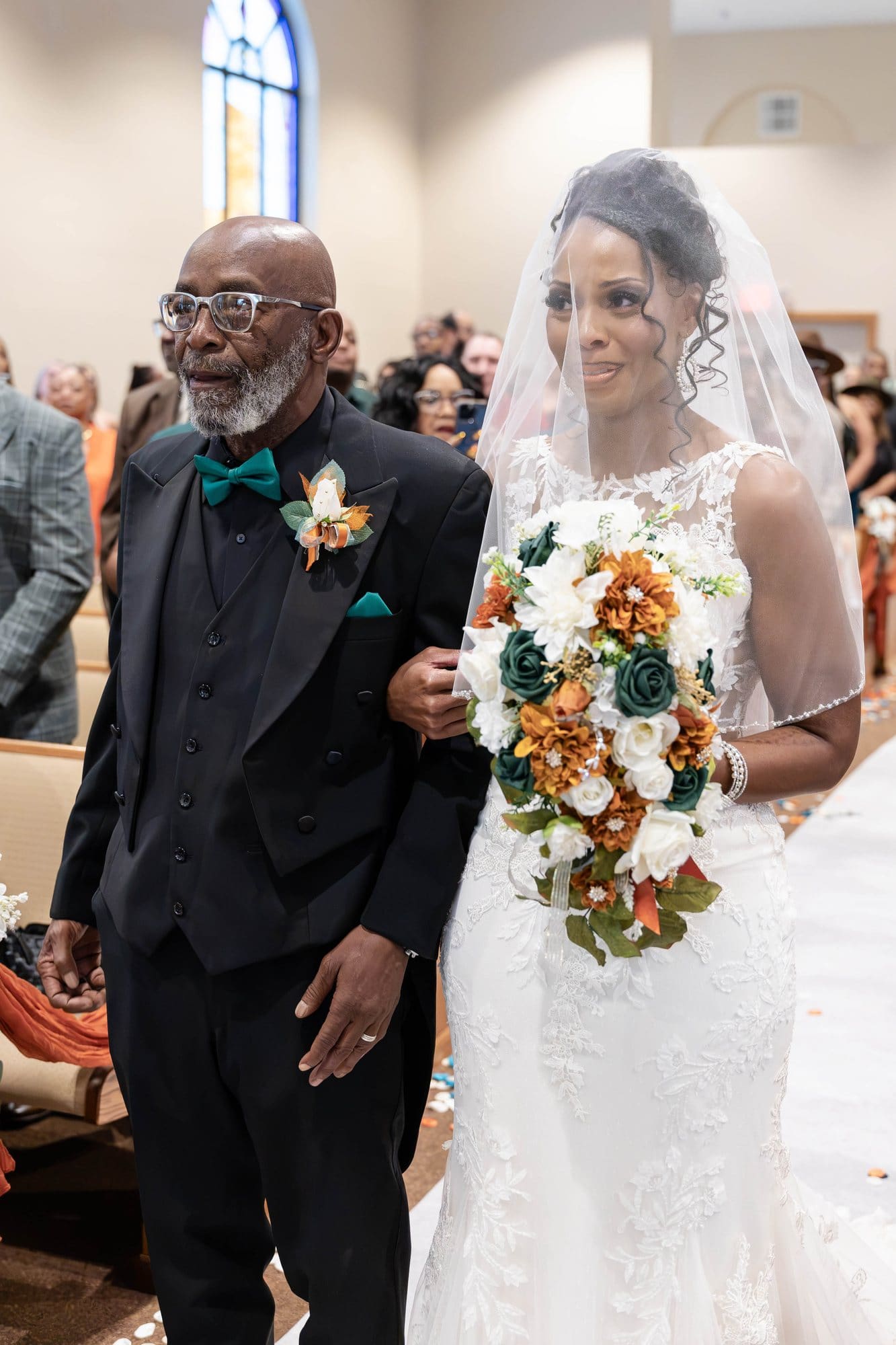 Nikeesha smiling behind her veil beside her father in a black suit and emerald bow tie