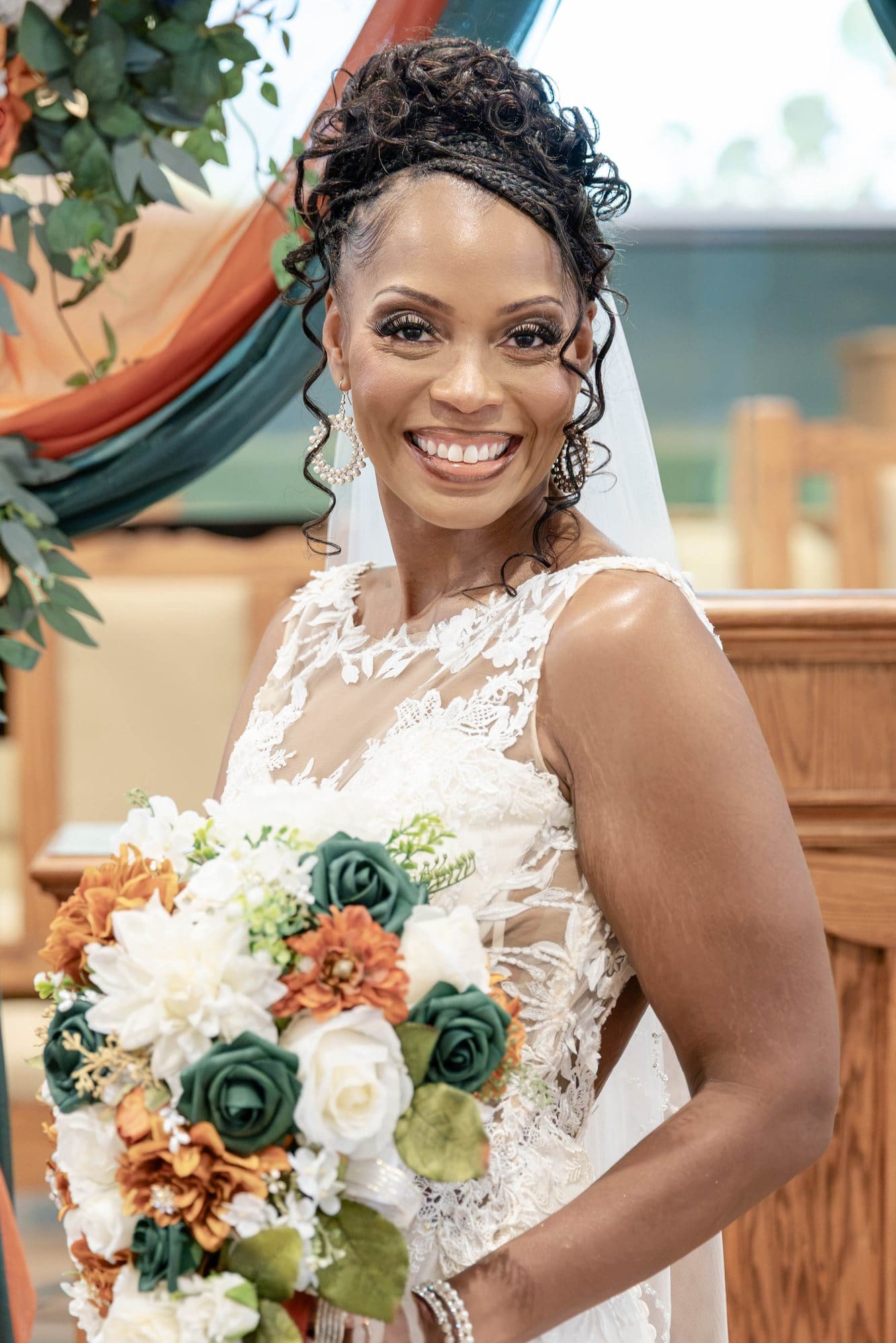 Nikeesha smiling over her shoulder with her copper and emerald bouquet in front of the altar
