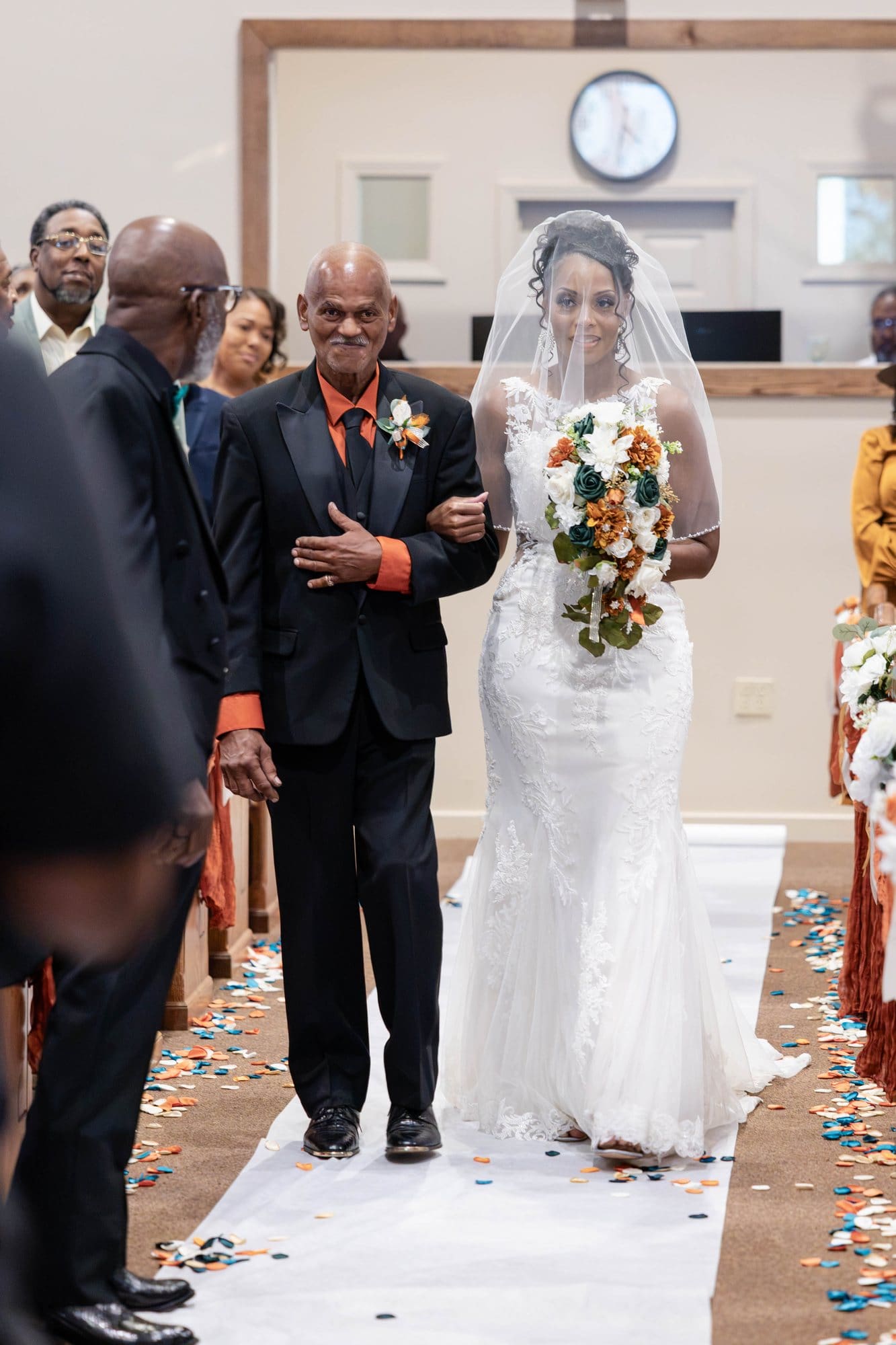 Nikeesha in her veil and ivory lace gown walking down the aisle between her father and stepfather