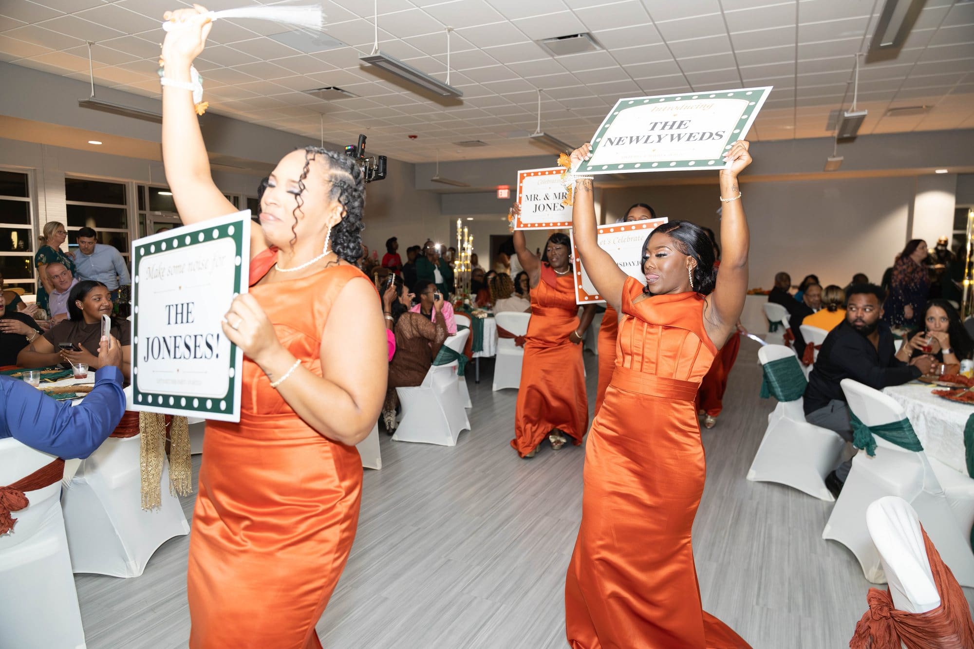Bridesmaids dancing into the reception holding marquee signs for the newlyweds