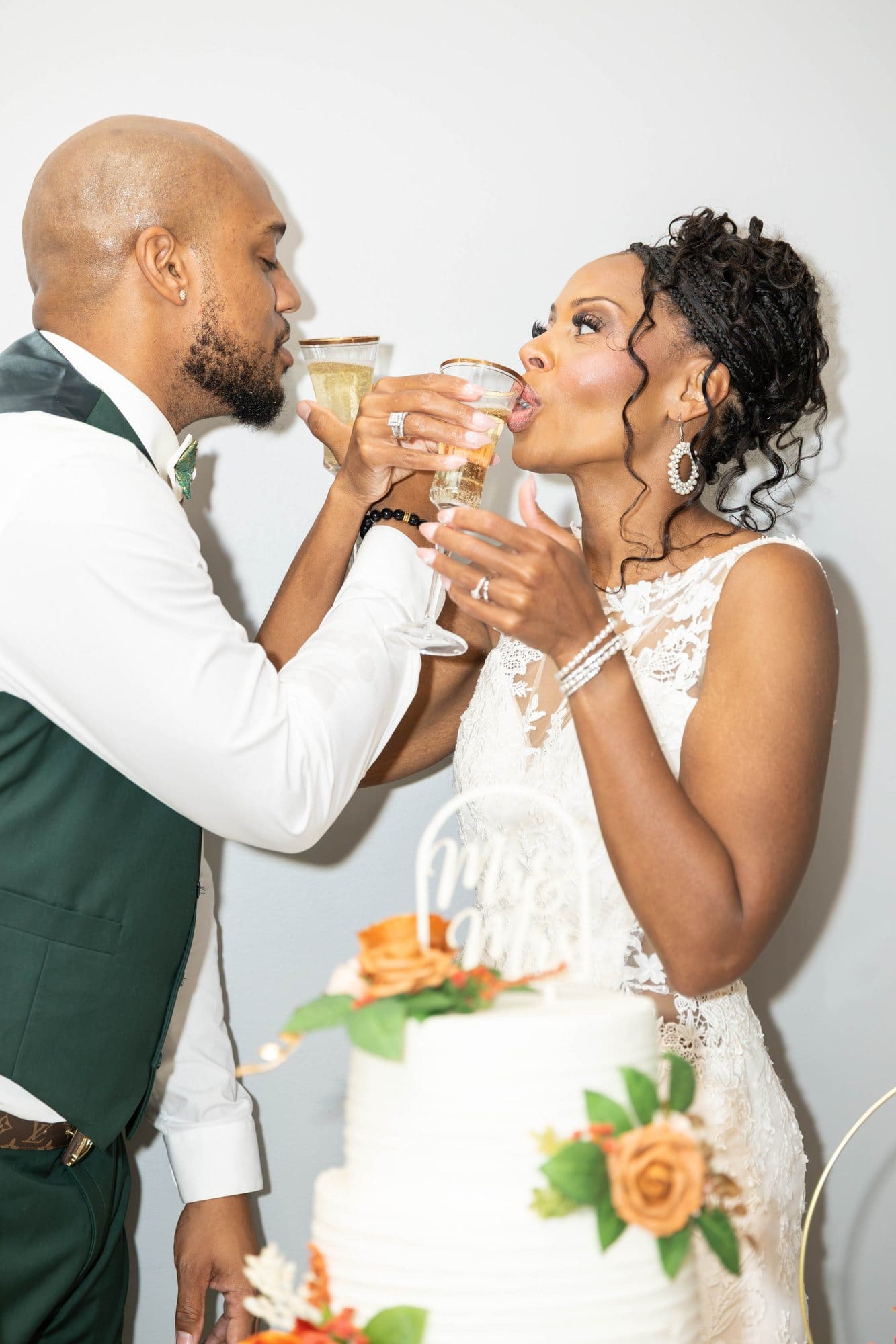 David and Nikeesha toasting with arms linked and gold-rimmed flutes beside their wedding cake