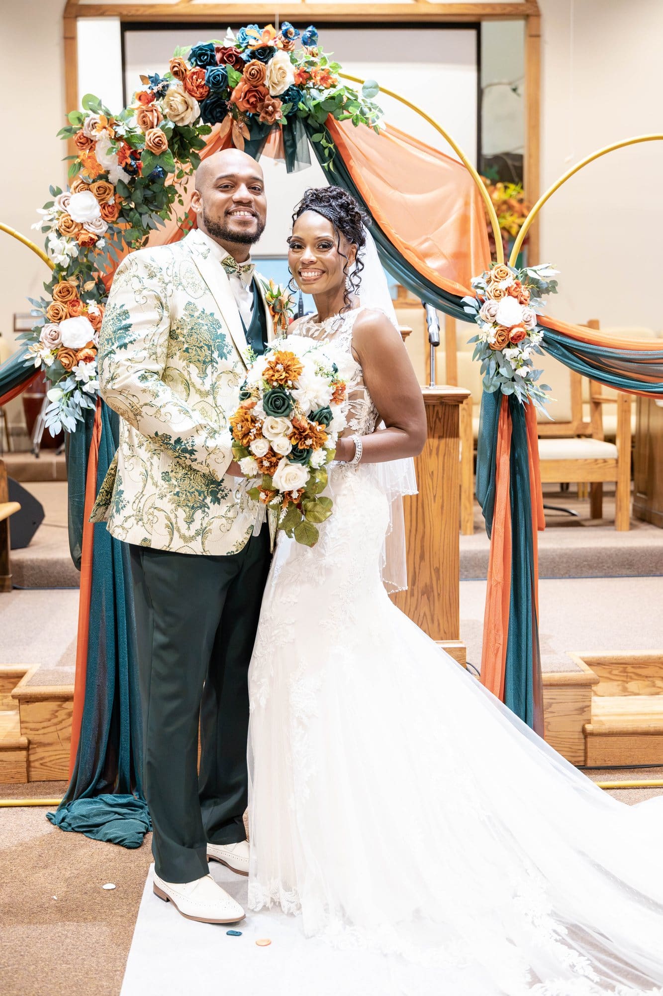 David and Nikeesha embracing at the altar in front of the gold hoops draped in emerald and copper
