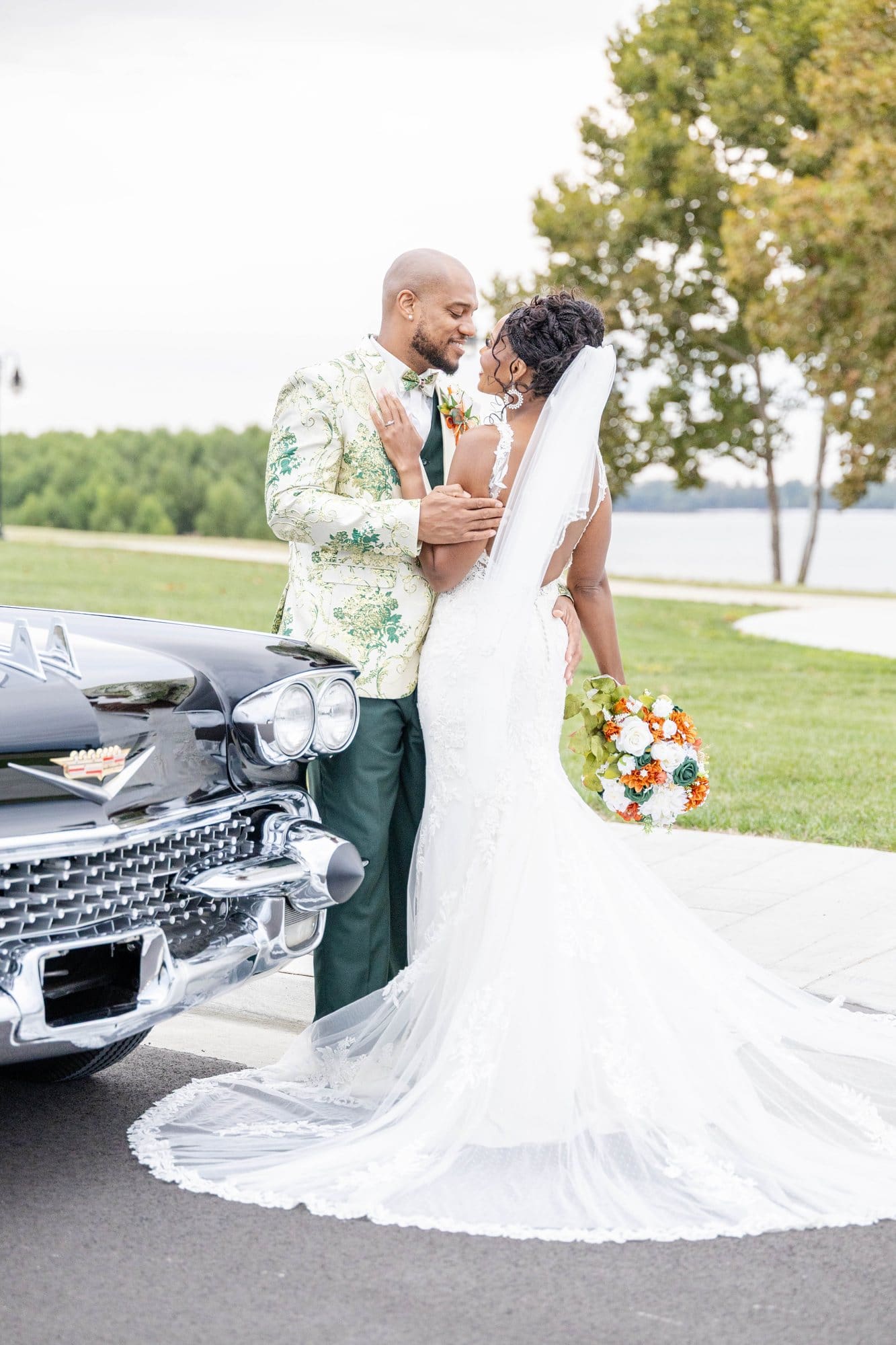 David and Nikeesha embracing beside the vintage Cadillac with her veil and train flowing on the Paducah riverfront