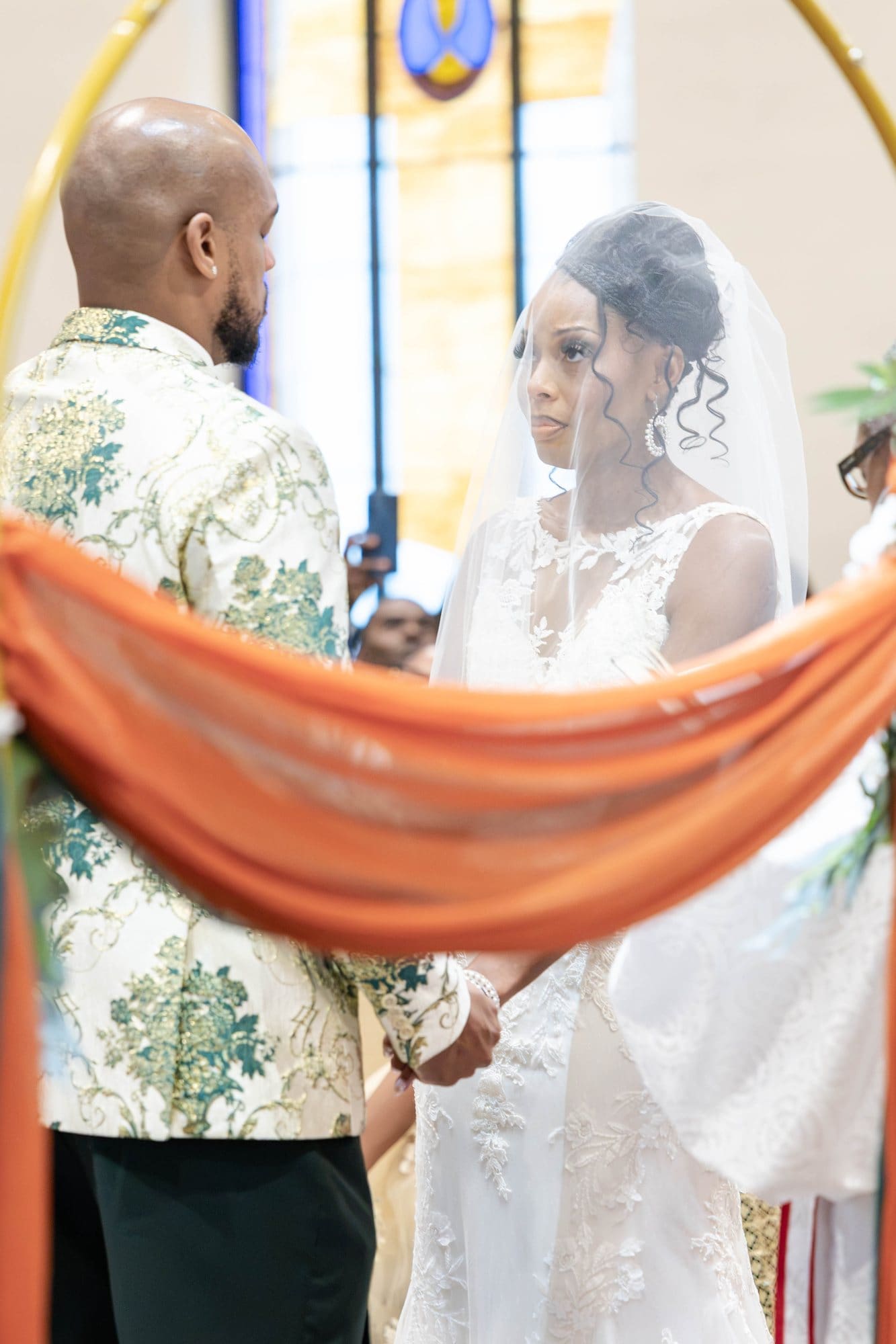 David and Nikeesha facing each other at the altar, seen through a copper drape on the gold hoop arch