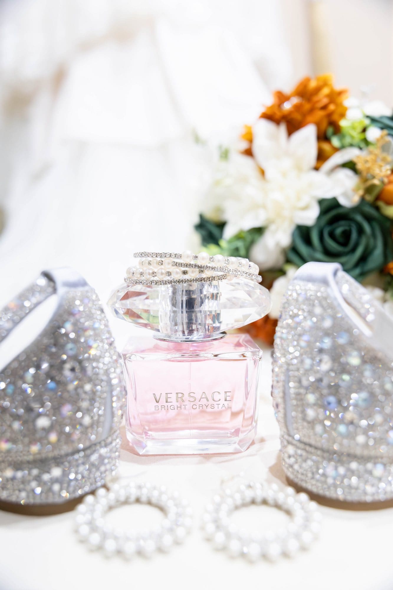 Crystal-embellished wedding shoes beside Versace Bright Crystal perfume and pearl earrings