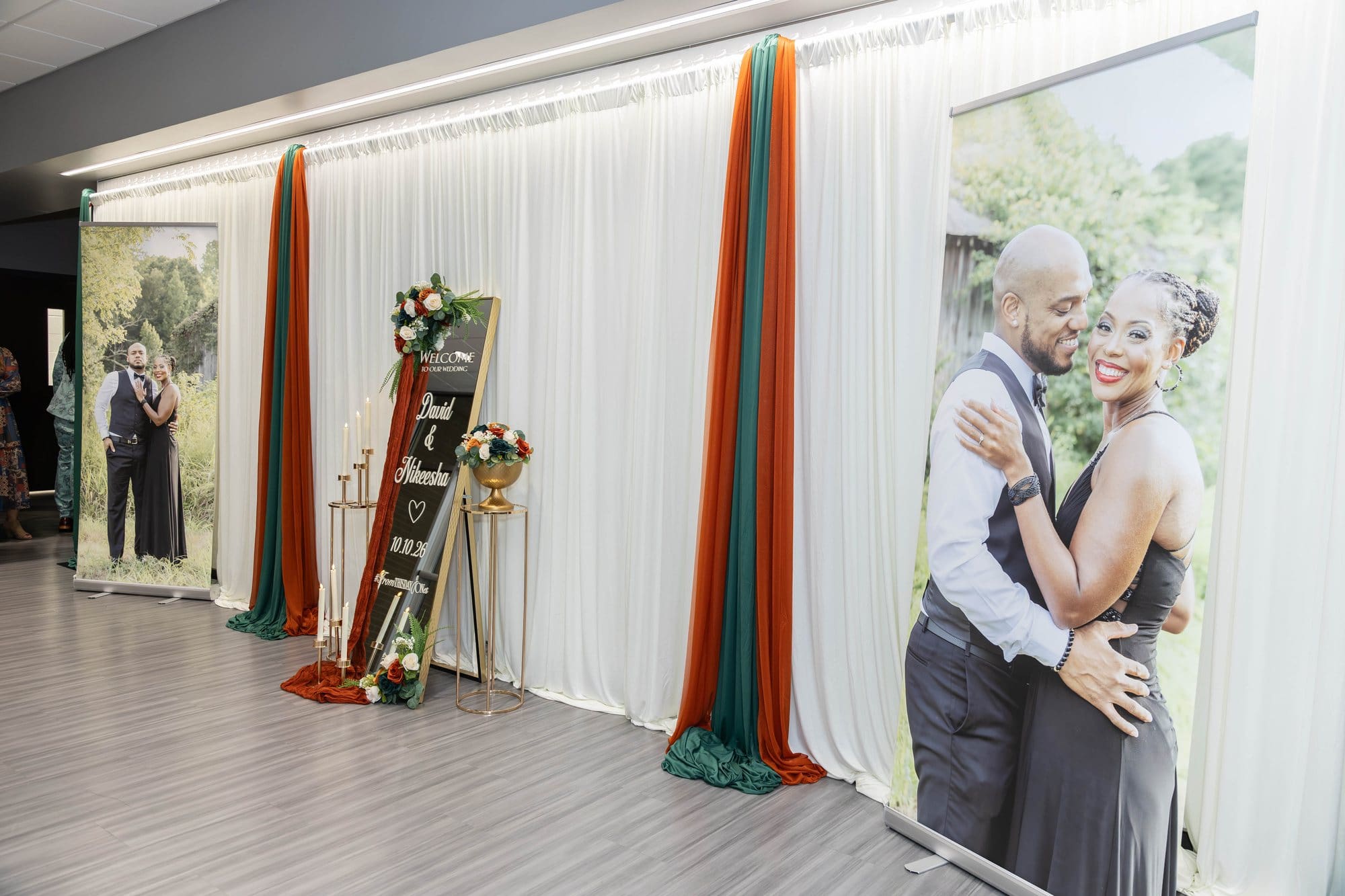 Two large engagement portraits of David and Nikeesha on banners beside a welcome mirror and copper and emerald draping at their Paducah, KY wedding reception