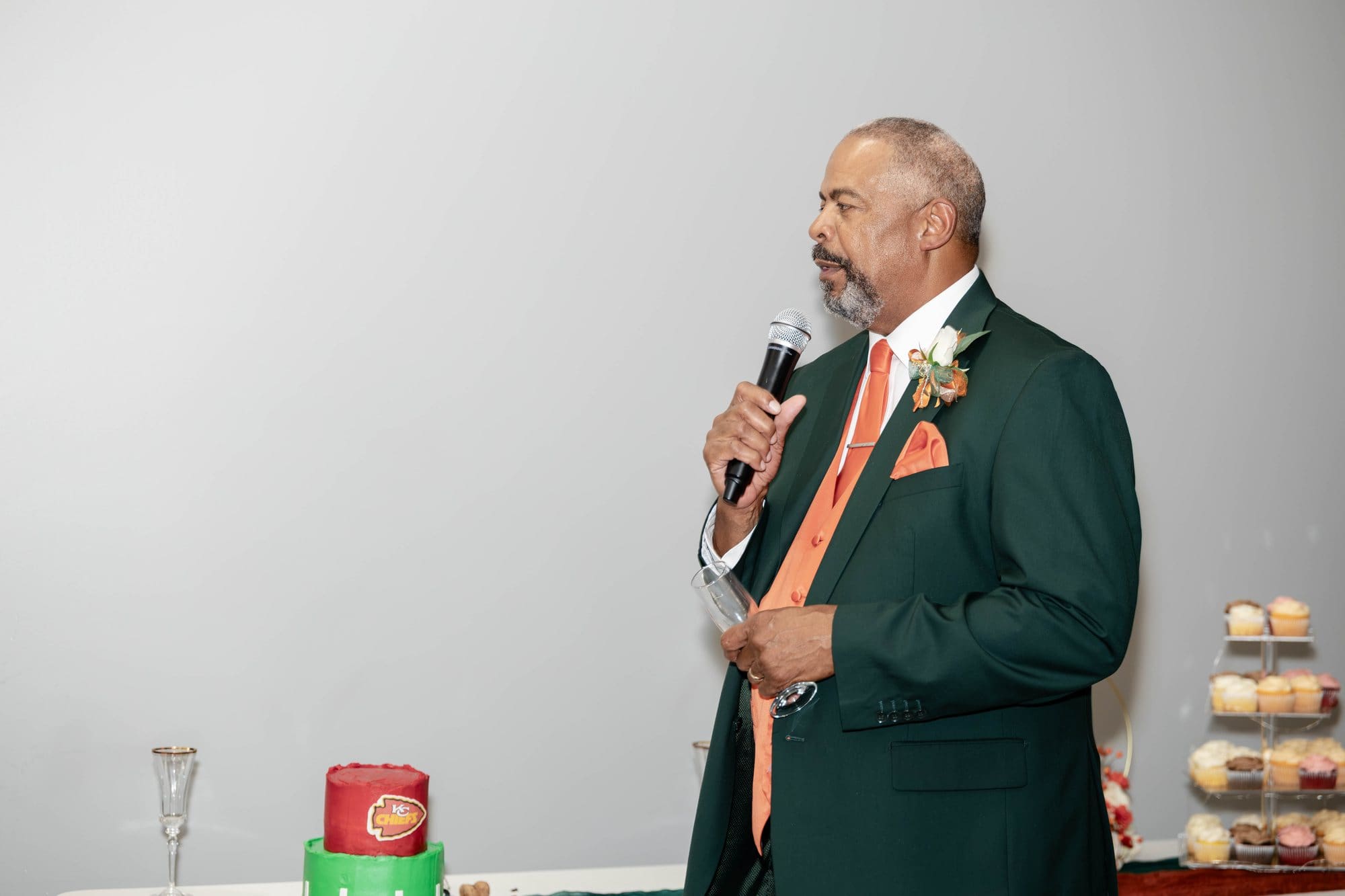 David's father in an emerald suit and copper tie speaking into the microphone during the reception toasts