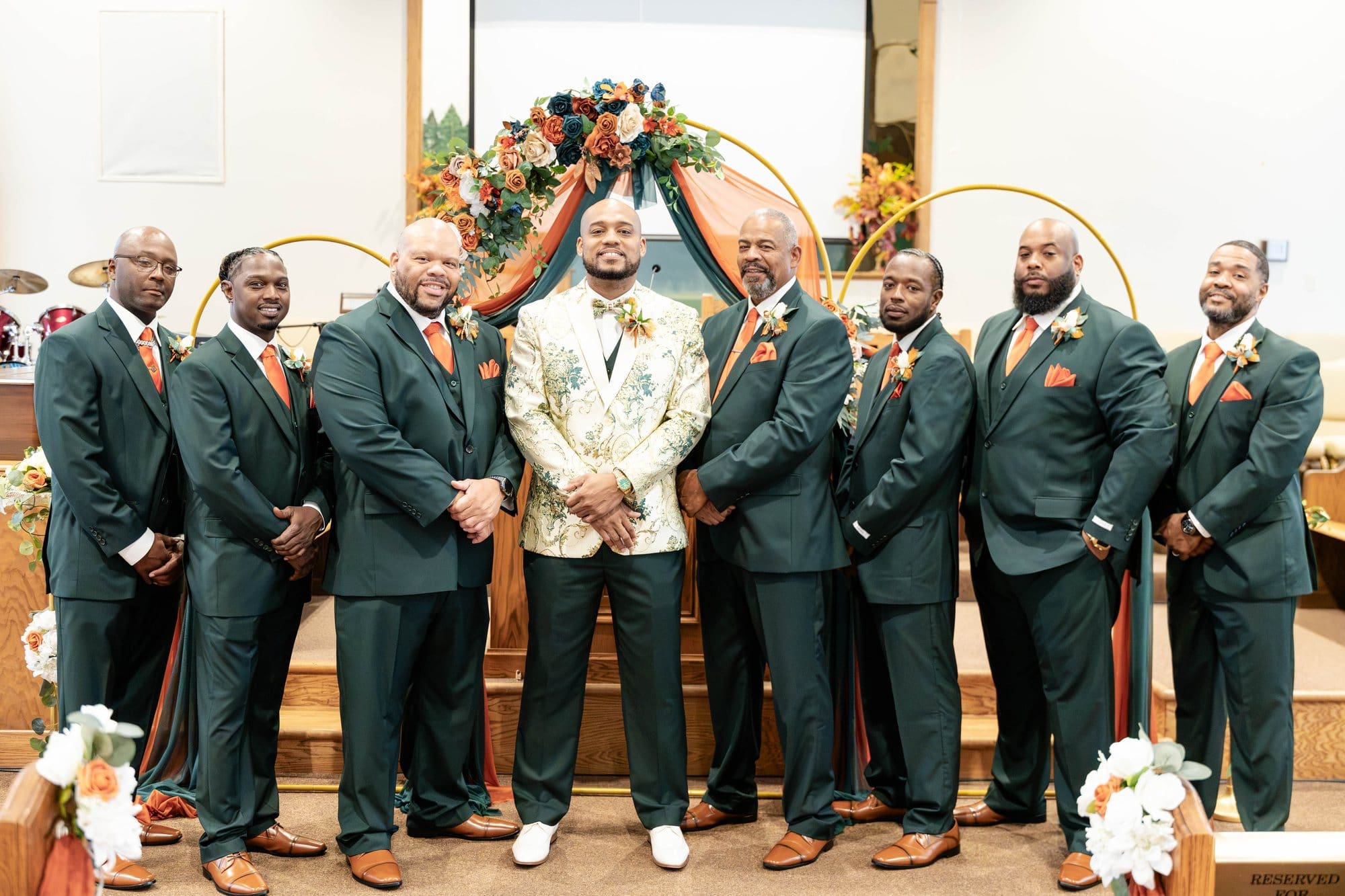 David with his groomsmen in deep emerald suits and copper ties in front of the gold hoop arch