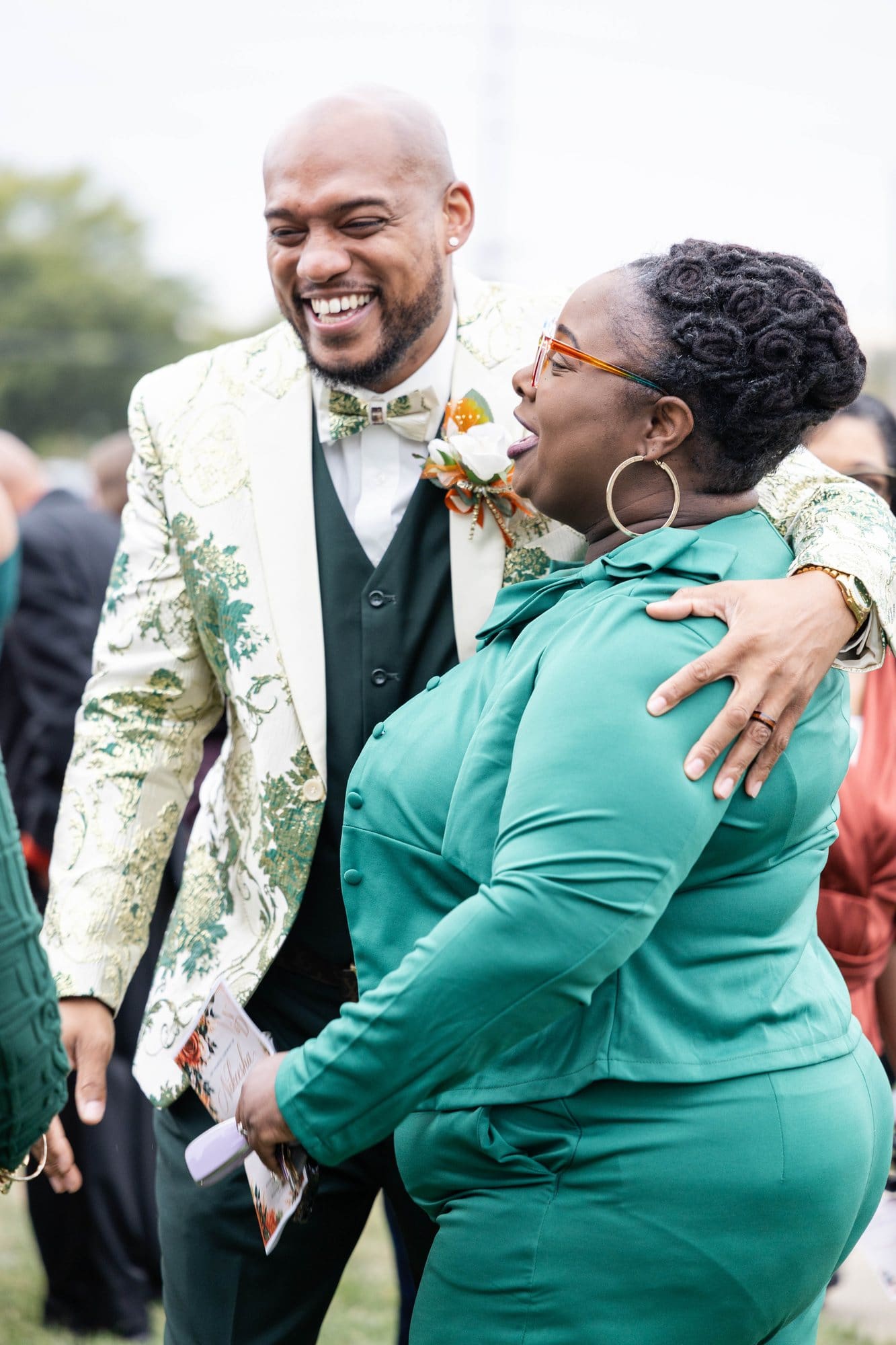 David laughing and hugging a guest in a green outfit outside the church