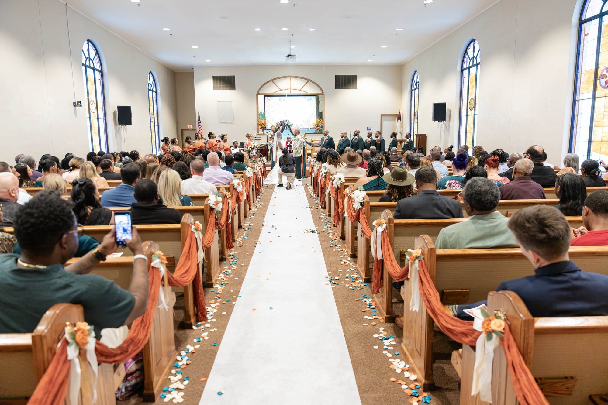 Guests filling the pews of the sanctuary and looking toward the white aisle runner scattered with petals before the ceremony