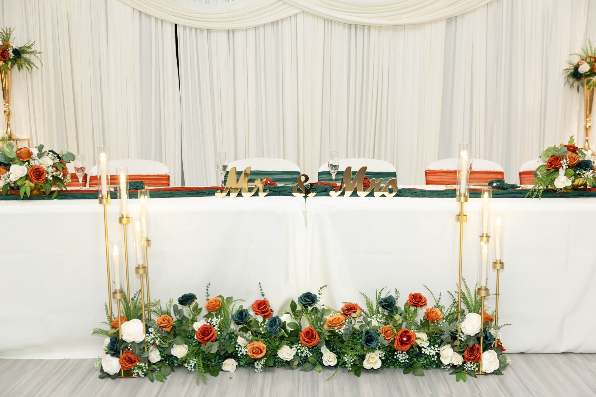Reception head table with gold Mr. & Mrs. letters, gold candle stands and copper, cream and emerald florals