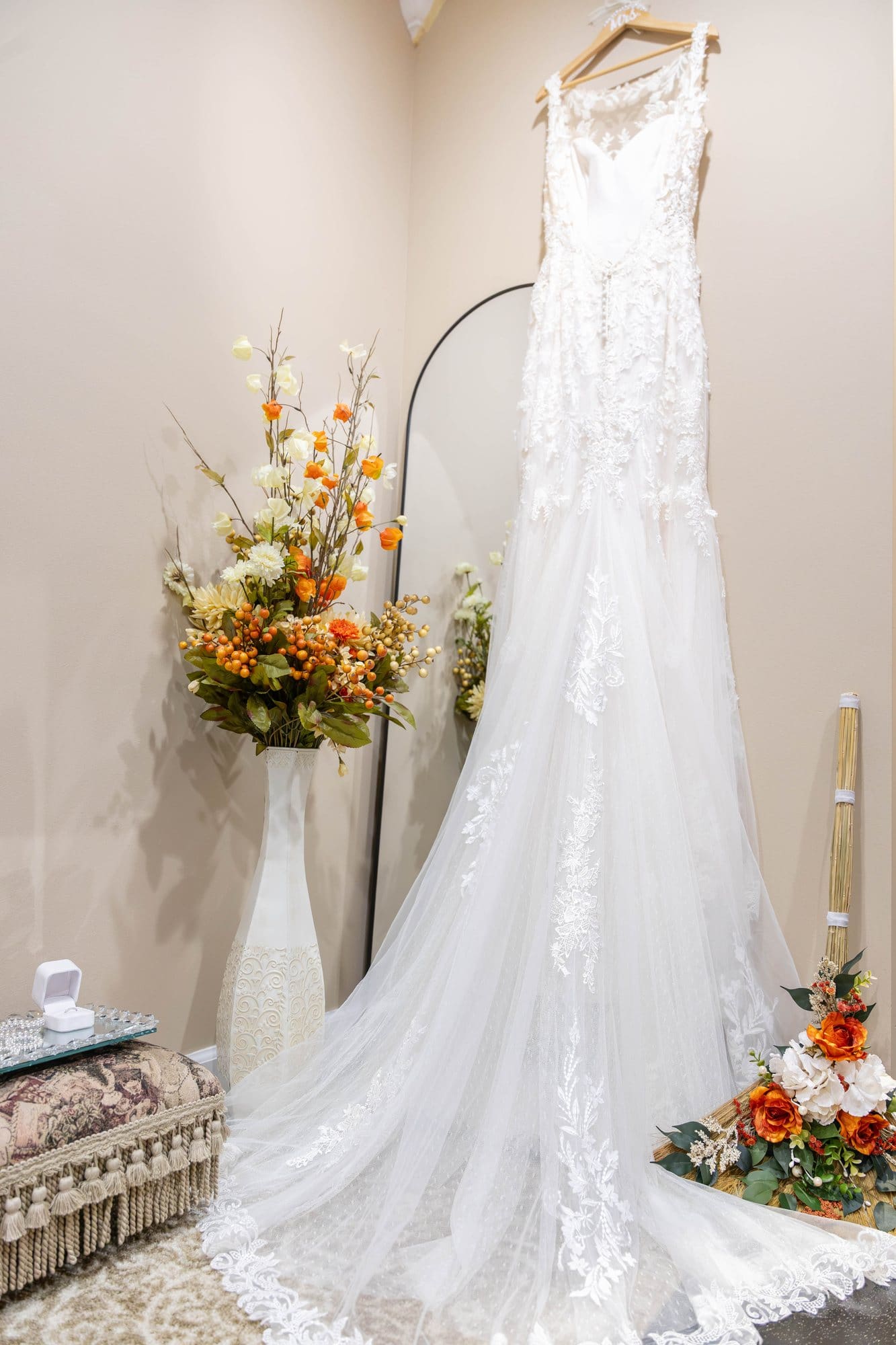 Ivory lace fit-and-flare wedding gown with a long tulle train hanging beside an arched mirror and fall florals