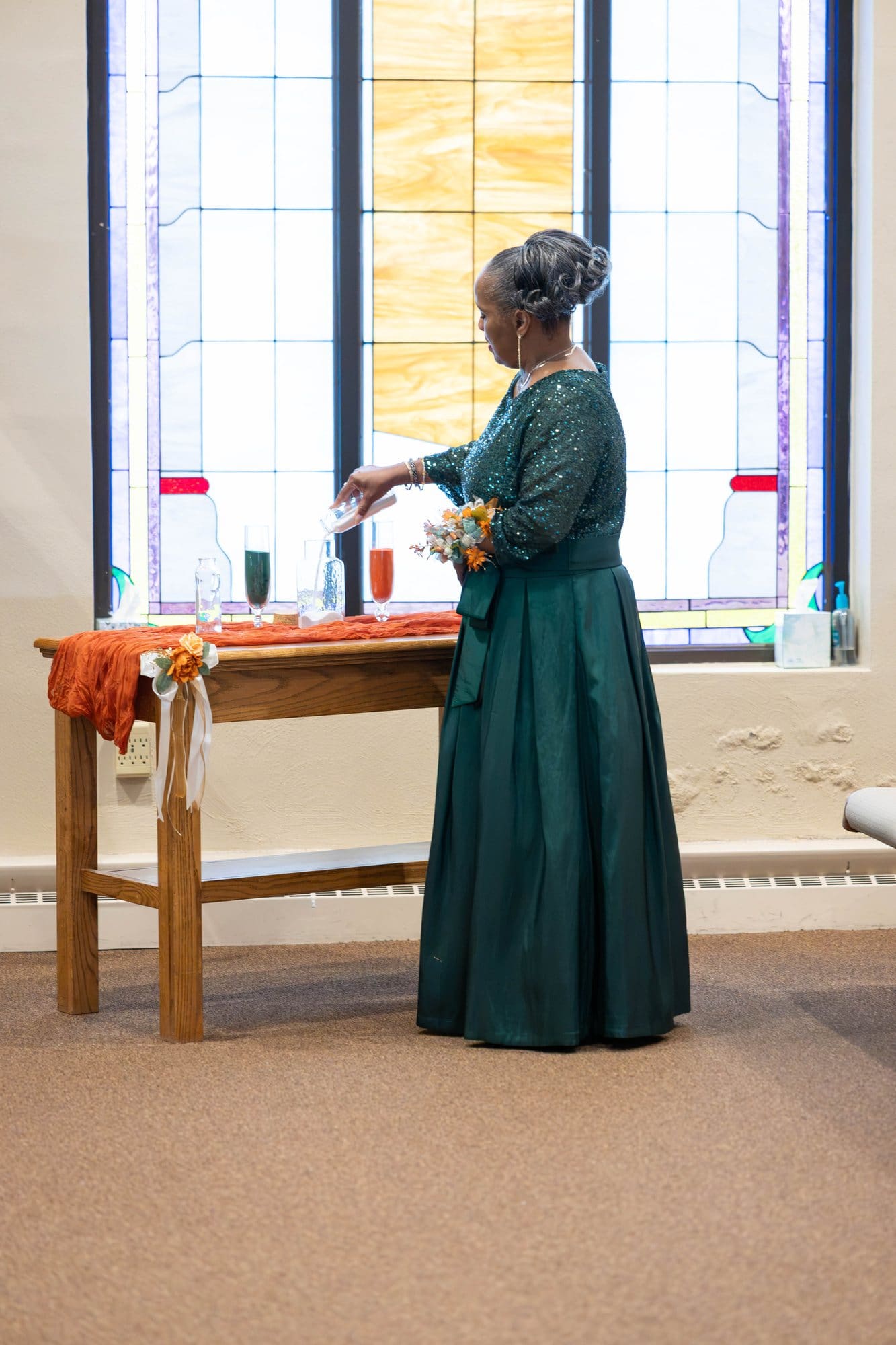 A mother of the couple in an emerald gown pouring the first layer of sand at the unity table