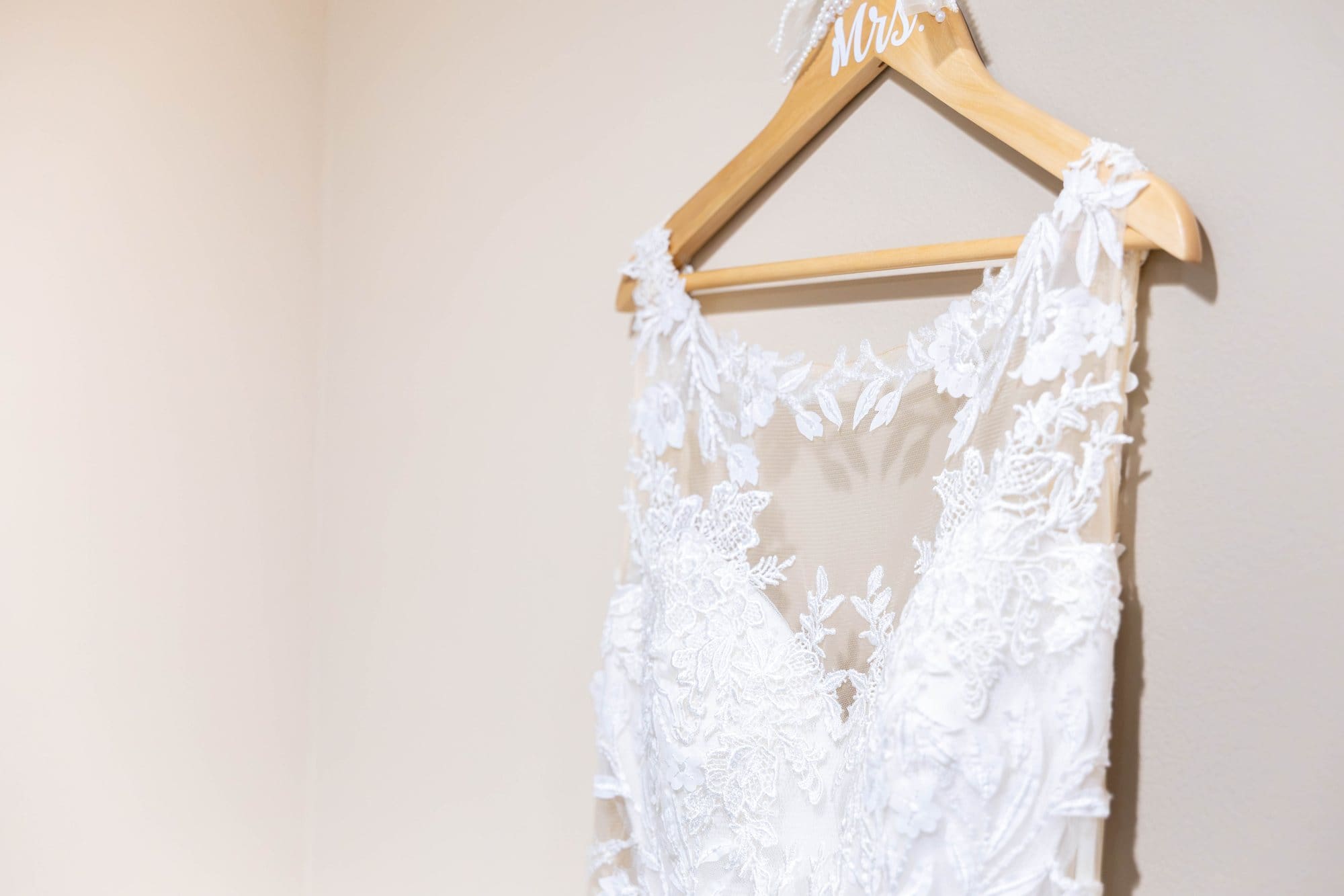 Lace bodice of an ivory wedding gown on a wooden hanger in a bridal suite at Destini's Salon