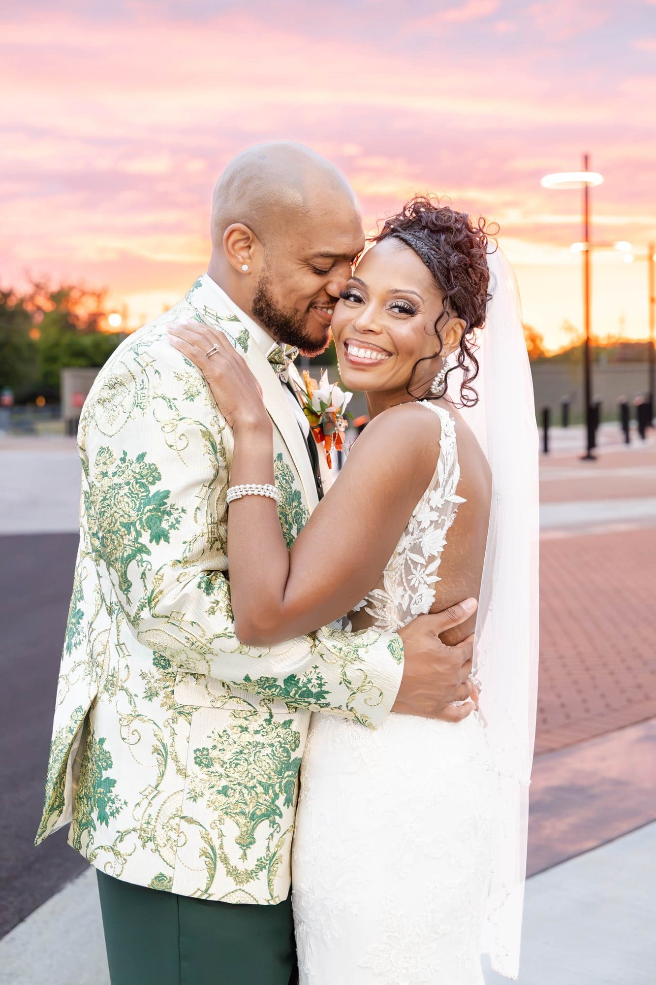 David and Nikeesha embracing and smiling at the camera with a pink and orange sunset glowing behind them