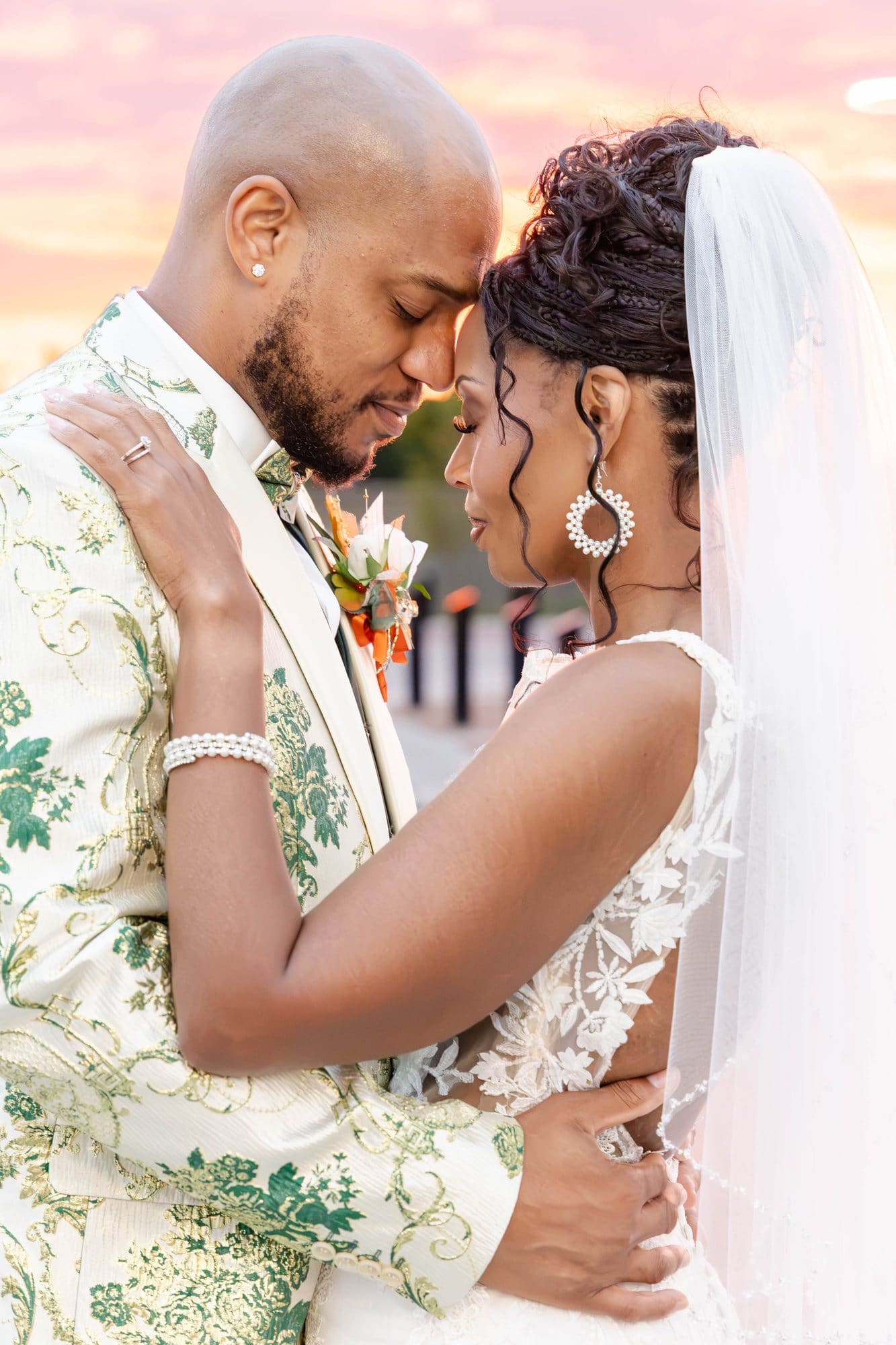 David and Nikeesha holding each other close, forehead to forehead, with a glowing pink and orange sunset behind them