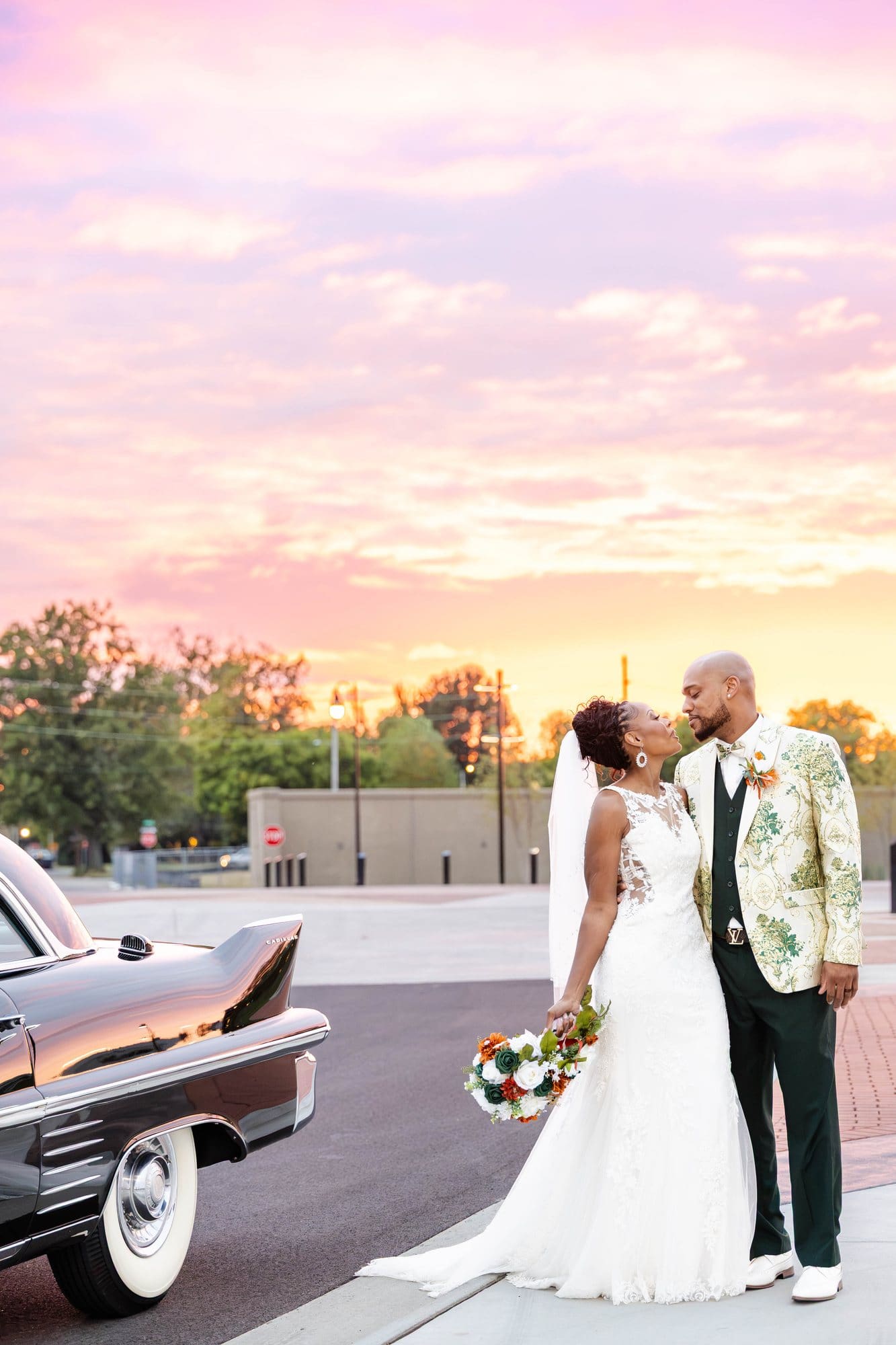 David kissing Nikeesha in front of a vintage Cadillac beneath pink and purple sunset clouds