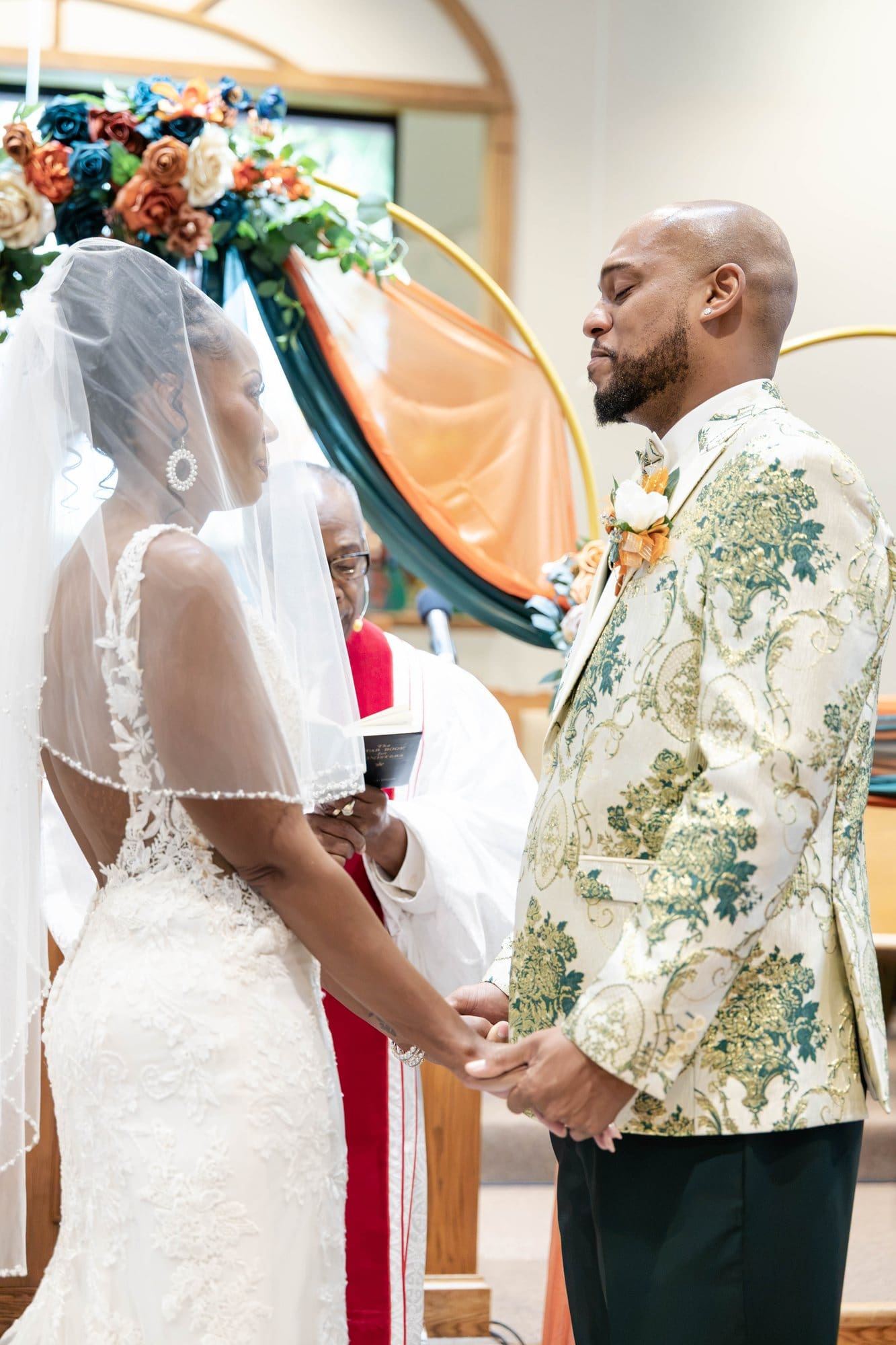 David and Nikeesha holding hands as Rev. Dr. Cole Sr. leads their vows beneath the floral arch
