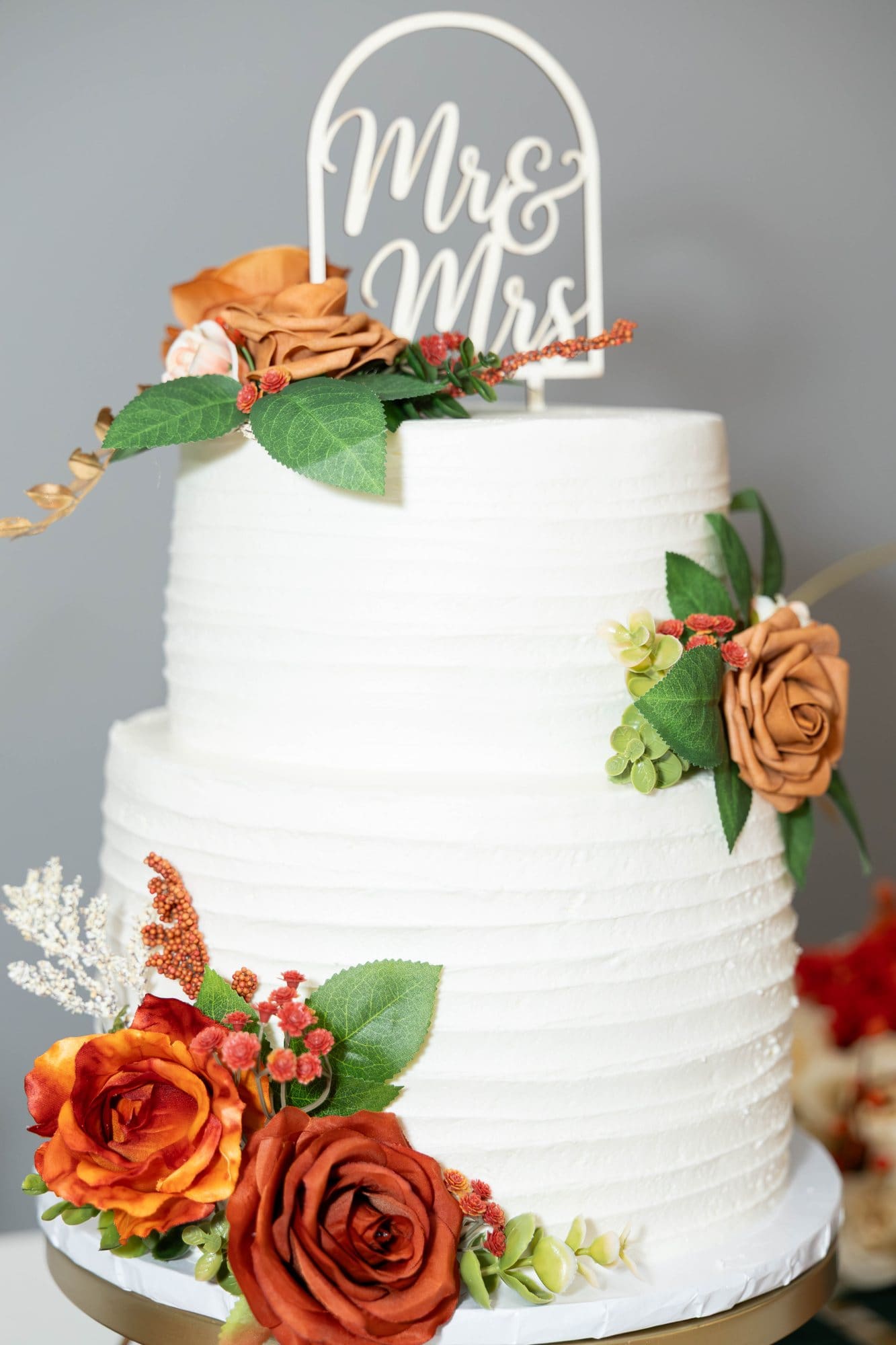Two-tier white buttercream wedding cake with a Mr & Mrs topper and copper and rust roses